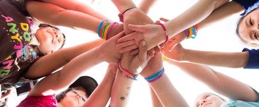 ways-to-participate-hero A circle of girls with their hands in for teamwork.